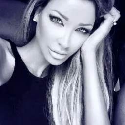 Portret kobiety z długimi, blond włosami i wyrazistym makijażem oczu, opierającej głowę na dłoni. Zdjęcie w chłodnej tonacji, ukazujące szczegóły twarzy i fryzury.