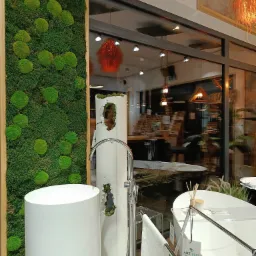 Nowoczesna łazienka z wolnostojącą umywalką cylindryczną, obok panel z mchu, w tle wanna i lampa wisząca.