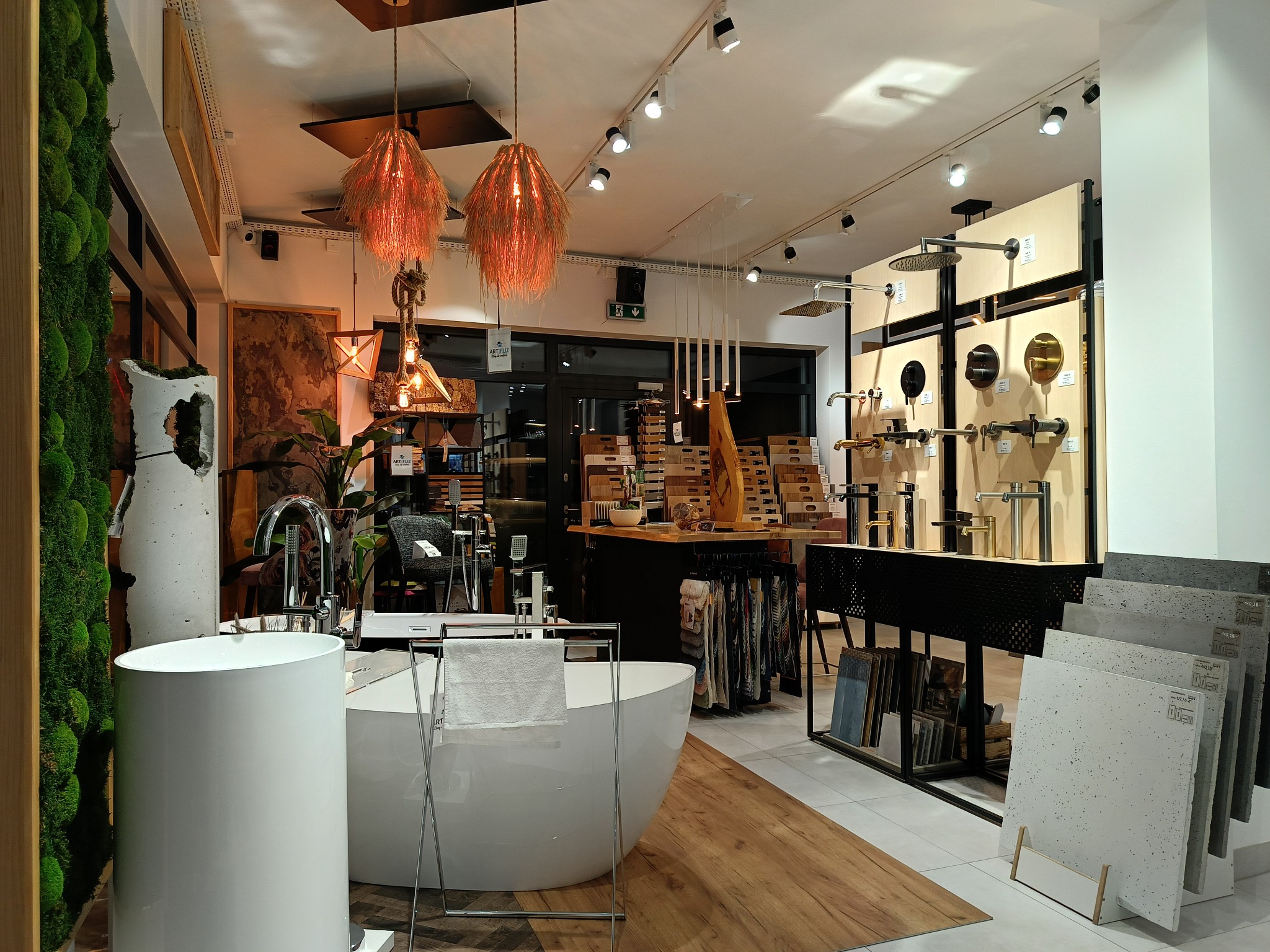 Ekspozycja armatury łazienkowej w salonie: wolnostojąca wanna z ręcznikiem, umywalka nablatowa, baterie, panele prysznicowe i oświetlenie dekoracyjne