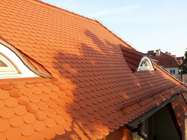 Czerwona dachówka karpiówka na dachu kamienicy z oknami typu wole oko, widok z góry na tle błękitnego nieba.