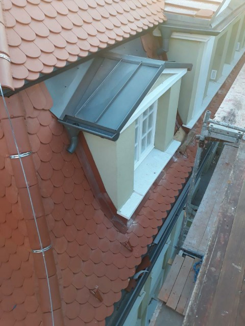 Fragment dachu z dachówką karpiówką i lukarną z metalowym pokryciem, widok z rusztowania w trakcie prac.