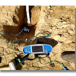 AVO technika sp z o o - Miernik w wykopie z przewodami, pomiar uziomu instalacji odgromowej. Widoczny fragment buta i narzędzia. Wyświetlacz miernika wskazuje wynik pomiaru.
