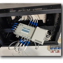 AVO technika sp z o o - Zamontowany multiswitch Terra w szafie rack z podłączonymi kablami koncentrycznymi, zabezpieczonymi niebieską taśmą. Widoczne gniazda zasilania w tle.