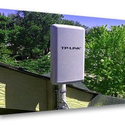 AVO technika sp z o o - Antena TP-Link zamontowana na dachu budynku, widoczne drzewa w tle. Biała obudowa anteny przymocowana do masztu za pomocą metalowych obejm.