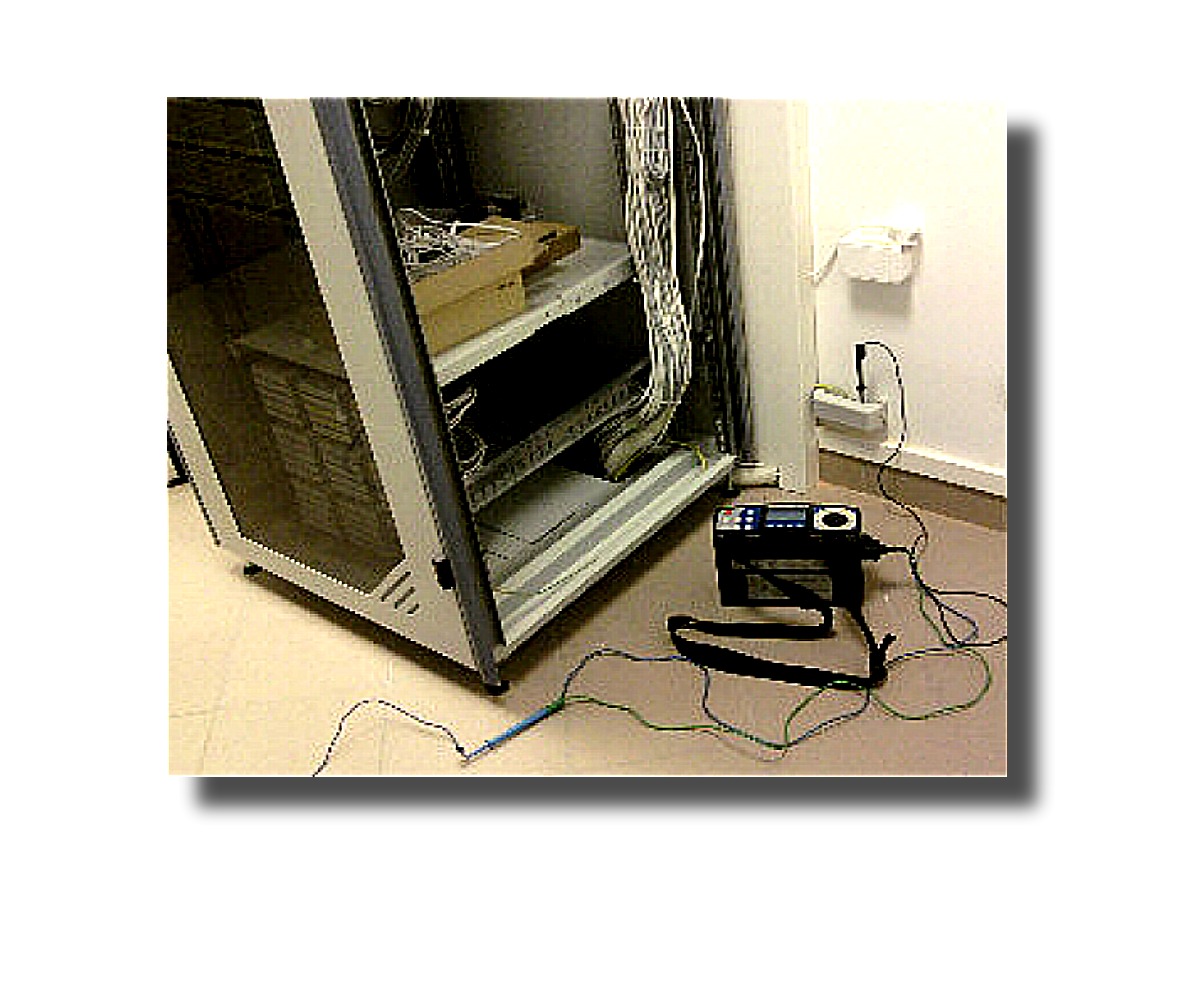 Otwarta szafa serwerowa z okablowaniem i miernikiem elektrycznym na podłodze, gniazdko elektryczne na ścianie. Pomiar instalacji w serwerowni.