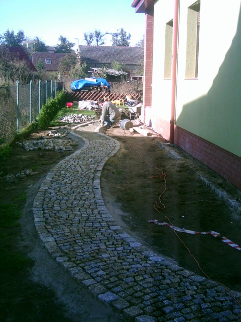 Układanie ścieżki z kostki granitowej w Lesznie. Widok na zakrzywiony fragment ścieżki w trakcie prac, z widocznym brukarzem i przygotowanym materiałem.