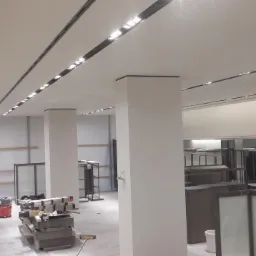 Nowoczesny sufit podwieszany z oświetleniem liniowym w lokalu handlowym, widok z dołu, Łodygowice. Minimalistyczny design, białe ściany i kolumny.