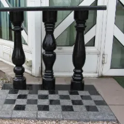 Balustrada z czarnego, polerowanego kamienia z ozdobnymi kolumnami, ułożona na szachownicy z jasnych i ciemnych płyt kamiennych przed wejściem do budynku.