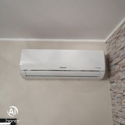 Euro-instal Piotr Ukleja - Biały klimatyzator Samsung Digital Inverter zamontowany na beżowej ścianie, obok fragmentu ściany wyłożonej dekoracyjnym kamieniem.