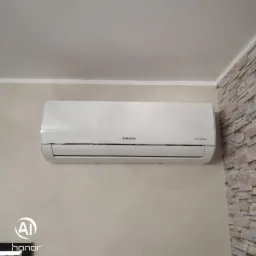 Biały klimatyzator Samsung Digital Inverter zamontowany na beżowej ścianie, obok fragmentu ściany wyłożonej dekoracyjnym kamieniem.