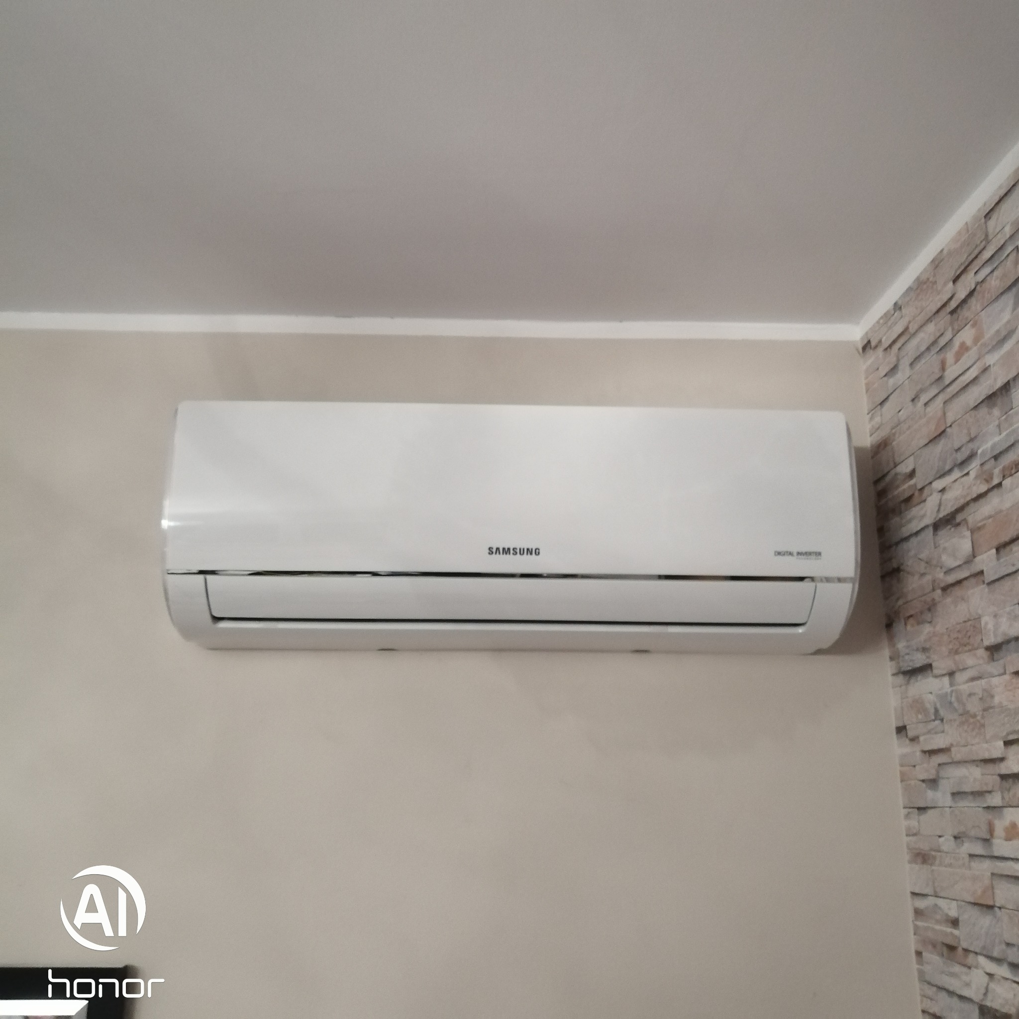 Biały klimatyzator Samsung Digital Inverter zamontowany na beżowej ścianie, obok fragmentu ściany wyłożonej dekoracyjnym kamieniem.
