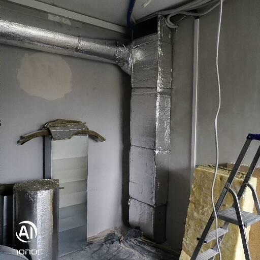 Izolowany kanał wentylacyjny pionowy i poziomy, drabina oparta o ścianę, rolka izolacji, surowy stan wykończenia wnętrza.