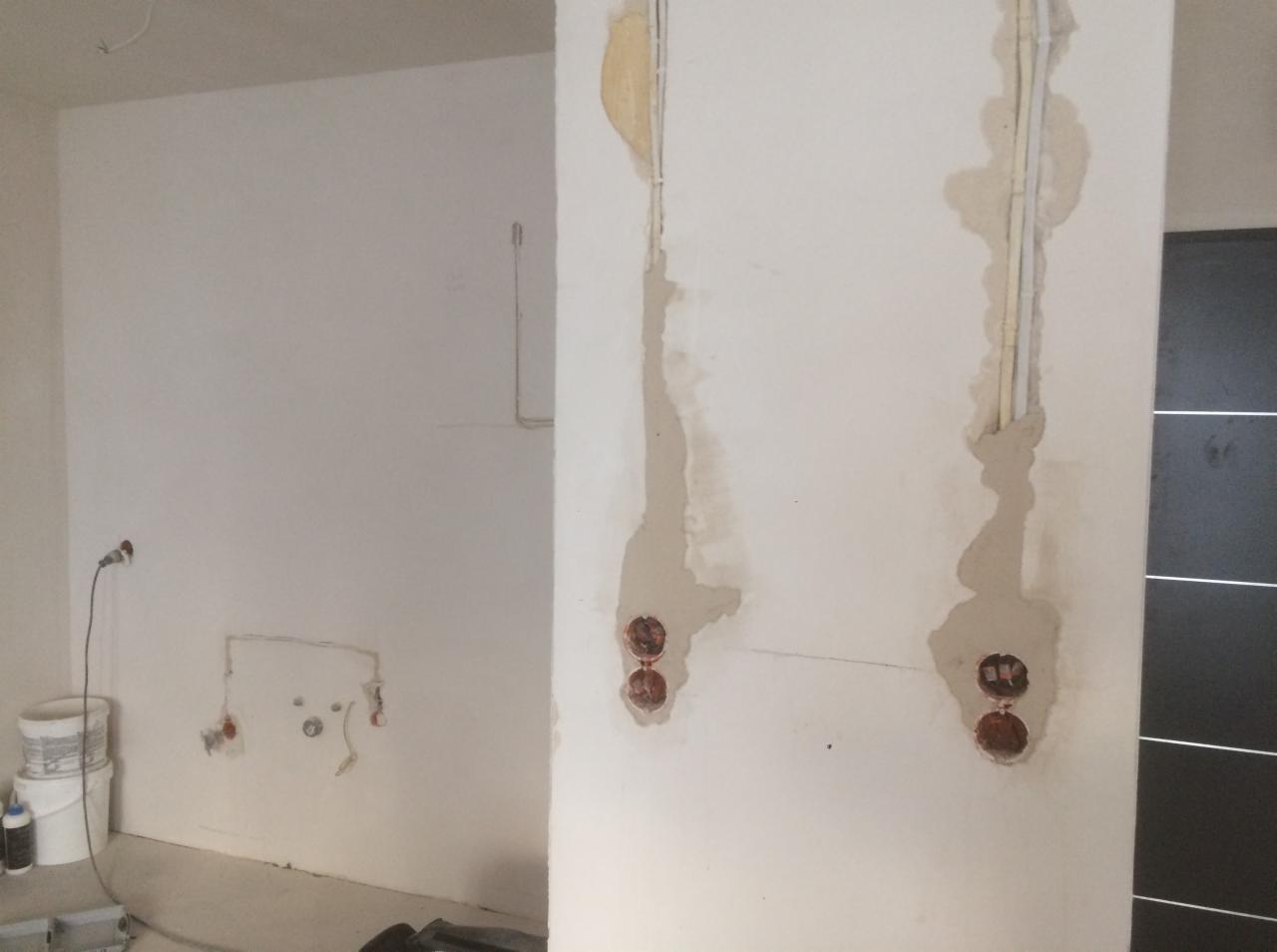 Przygotowanie do instalacji elektrycznej w nowym mieszkaniu: wyżłobione bruzdy w ścianie, widoczne przewody i puszki pod gniazdka, ślady po gipsowaniu, białe ściany w surowym stanie.