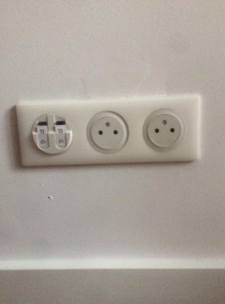 Blok potrójnego gniazdka elektrycznego na białej ścianie, z dwoma standardowymi gniazdkami europejskimi i jednym gniazdkiem telefonicznym, sfotografowane z bliska.