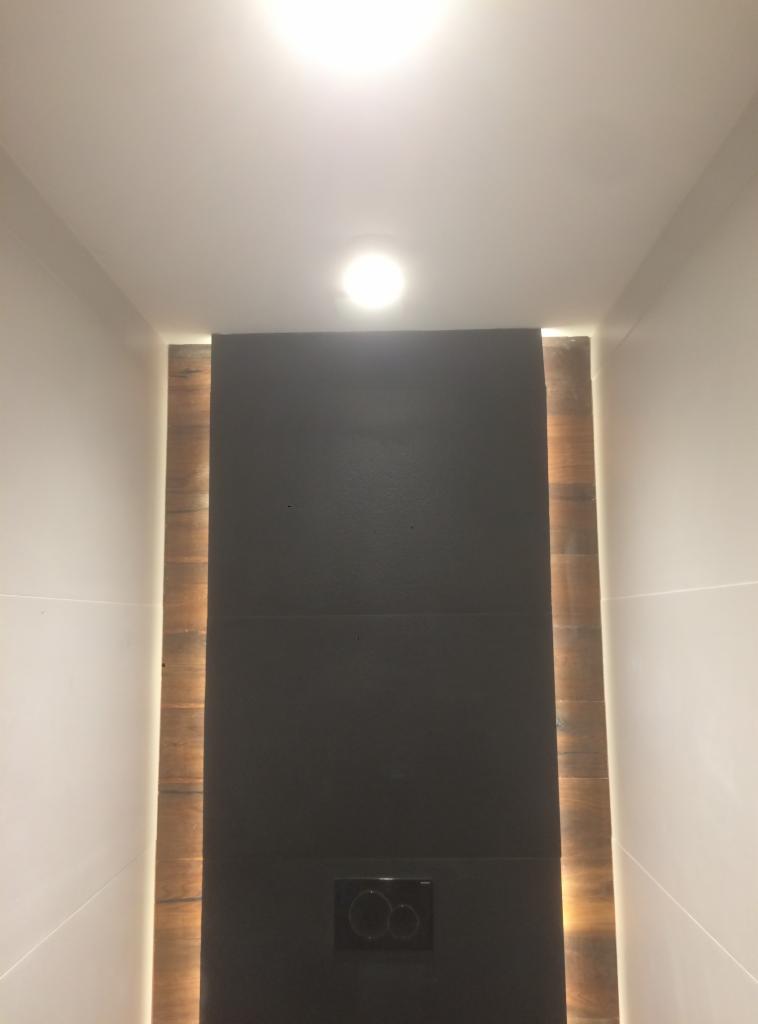 Nowoczesna toaleta podtynkowa z czarną płytą i drewnianym akcentem z podświetleniem LED, zamontowana w łazience w Wysogotowie.