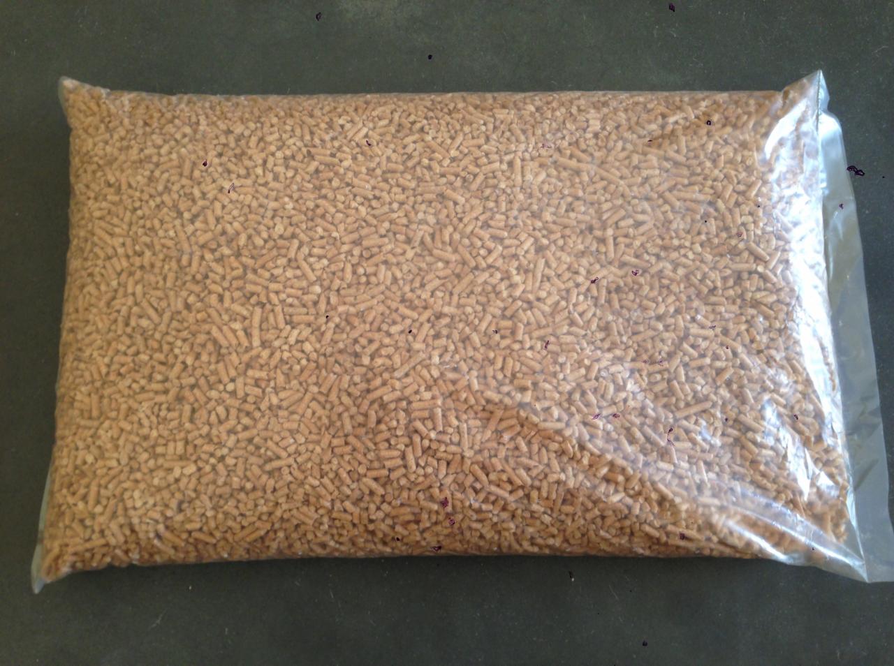 Wypełniony pelletem worek foliowy, leżący na ciemnej powierzchni. Widoczne drobne, jasnobrązowe granulki pelletu. Pakowanie gotowe do transportu lub składowania.