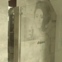 Szklana kabina prysznicowa z grafiką kobiety w stylu retro, zamontowana w łazience wykończonej płytkami imitującymi kamień.