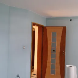 Świeżo pomalowane na błękitno wnętrze pokoju z drewnianymi drzwiami z przeszkleniami, widoczny wałek malarski.