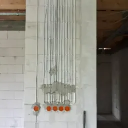 Ściana z betonu komórkowego z pionowo ułożonymi przewodami elektrycznymi w bruzdach, częściowo zamaskowanymi zaprawą, oraz puszkami instalacyjnymi w kolorze pomarańczowym.