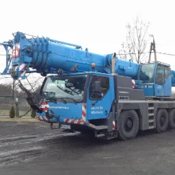 Niebieski dźwig Liebherr na błotnistym terenie; widoczne numery kontaktowe i adres strony www.dźwigisosnowiec.pl. Sprzęt budowlany w gotowości.