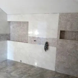 Wykończona łazienka z szarymi płytkami w dwóch odcieniach, mozaika w strefie prysznicowej z wnęką, białe płytki na ścianach, szare płytki podłogowe, ręcznik wiszący na ścianie.