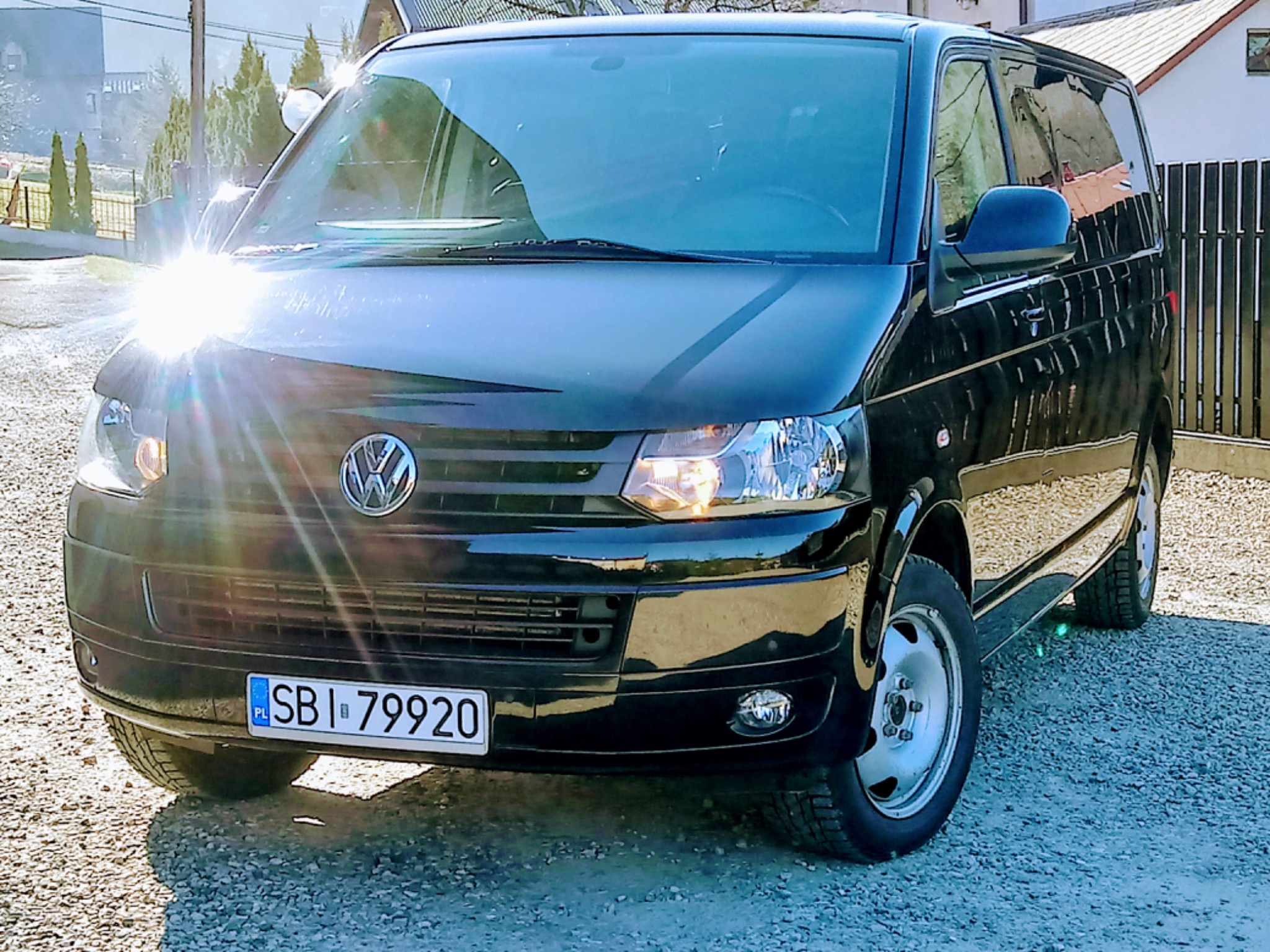 Czarny Volkswagen Transporter T5 z polską tablicą rejestracyjną SBI 79920, zaparkowany na żwirowej drodze, z odbiciem słońca na masce.