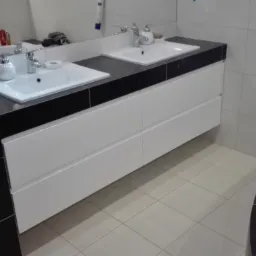 Łazienka z dwoma umywalkami nablatowymi na białej szafce z czarnym blatem, widok z boku na fragment wanny.