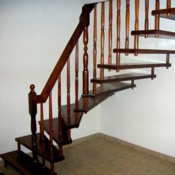 Wood & Iron Manufacture - Kaskadowe, drewniane schody dywanowe w ciemnym odcieniu, z toczonymi balustradami. Stopnie bez podstopnic, mocowane do ściany. Widok z dołu, na jasnym tle.