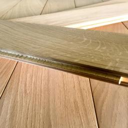 Wood & Iron Manufacture - Fragment podłogi z desek dębowych, z widocznym systemem łączenia na pióro i wpust. Jasne drewno, ciepłe oświetlenie, zbliżenie na strukturę i detale wykończenia.