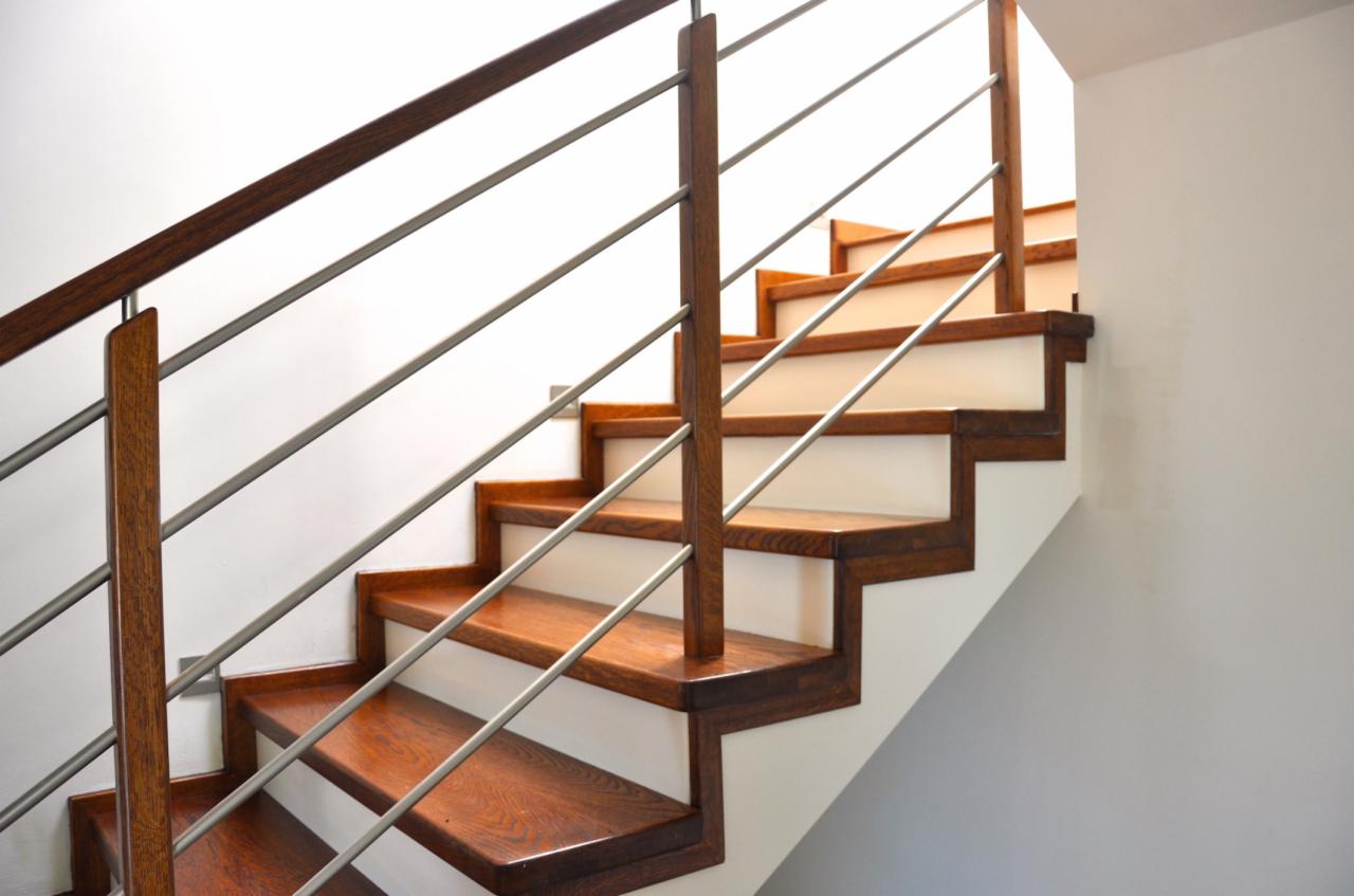 Nowoczesne schody z drewnianymi stopniami i metalową balustradą, widok z dołu, jasne wnętrze, minimalistyczny design, naturalne światło podkreśla ciepło drewna.