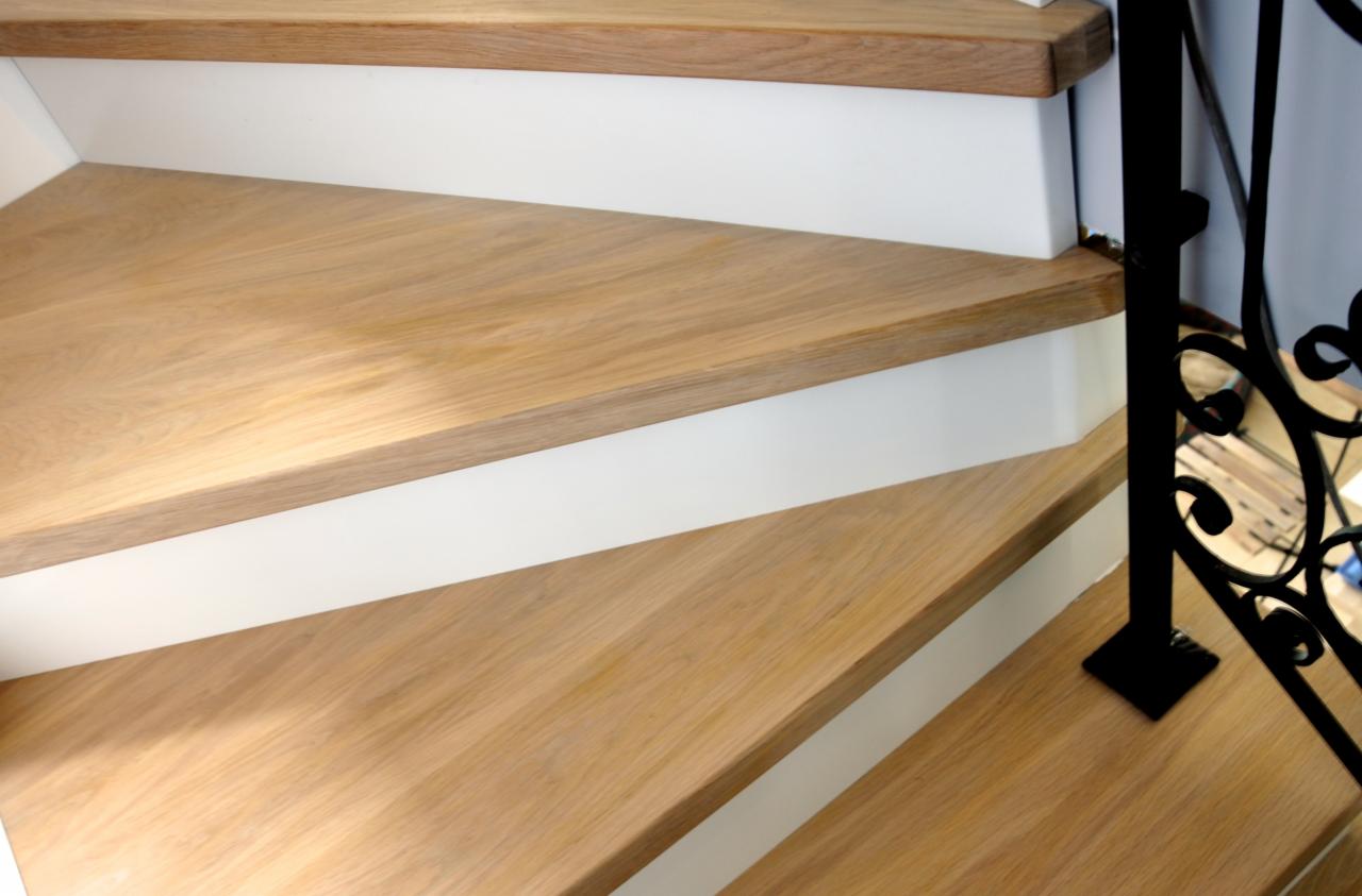 Jasne, drewniane schody z białymi podstopnicami i czarną, ozdobną balustradą. Ujęcie z dołu, podkreślające detale wykończenia i wzór drewna.