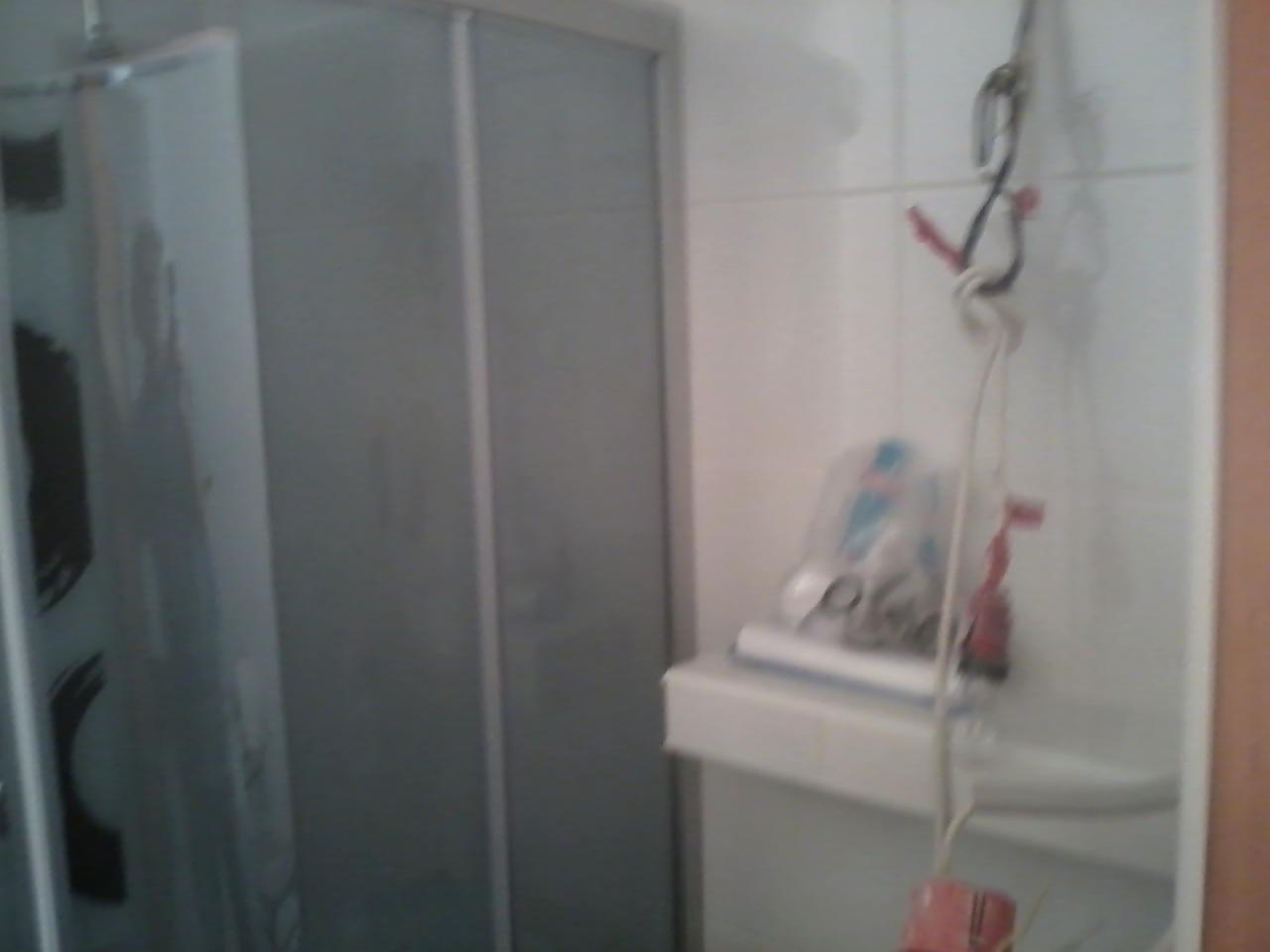 Niedokończona łazienka z kabiną prysznicową i półką z kosmetykami, widoczne przewody i narzędzia wiszące na ścianie.