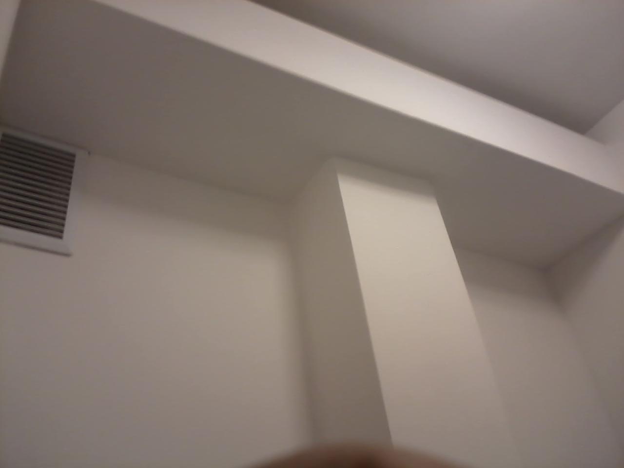 Wnętrze z pomalowanymi na biało ścianami, widoczny fragment kolumny, sufitu i kratki wentylacyjnej.