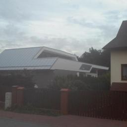 P.H.U. MAGIC ŁUKASZ GÓRKA - Nowoczesny dom z unikalnym dachem z blachy na tle pochmurnego nieba, widoczny zza drewnianego ogrodzenia.