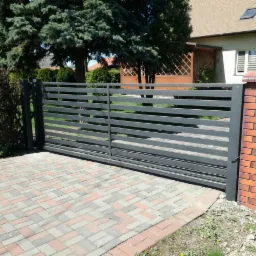 Nowoczesna, przesuwna brama wjazdowa z poziomych profili stalowych, zamontowana na posesji z kostką brukową i ceglanym słupkiem.