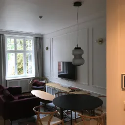 Salon w Gdańsku z elementami systemu inteligentnego domu: dotykowy panel sterowania na ścianie i wisząca lampa. W tle widoczny telewizor i meble.