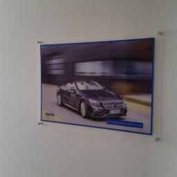 XMEDIA Agencja Reklamowa Marta Zaręba - Plakat reklamowy w przezroczystej ramie, przedstawiający czarny kabriolet Mercedes-Benz na drodze, z logo firmy Fortatech i napisem 'A company of the RUGG Group'.