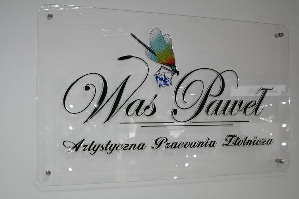 Elegancka, szklana tablica z logo firmy Was Paweł Artystyczna Pracownia Złotnicza. Logo zdobi kolorowa ważka i diament.