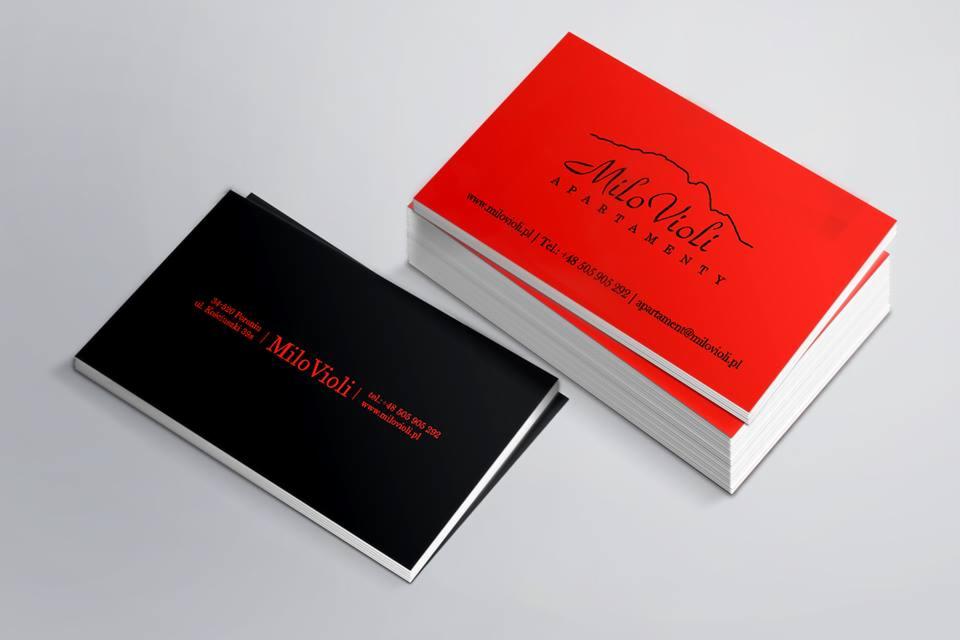Stos czerwonych wizytówek Milo Violi z czarnym logo i danymi kontaktowymi obok pojedynczej czarnej wizytówki z czerwonym tekstem na jasnym tle.