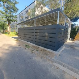 DanTe - Nowoczesna zabudowa śmietnikowa z szarego drewna i metalowej siatki, na tle bloku mieszkalnego i zieleni. Widok z poziomu chodnika, w słoneczny dzień.