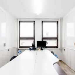 Jasne, minimalistyczne wnętrze biura z długim stołem konferencyjnym, białymi szafami w zabudowie i oknami z widokiem na miasto. Elementy wyposażenia biurowego na stole.