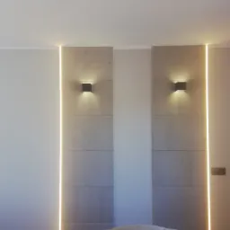 Nowoczesna ściana w sypialni z panelami imitującymi beton, oświetleniem LED w pionowych szczelinach i minimalistycznymi kinkietami.