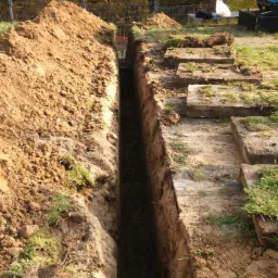 Wykop liniowy w Bydgoszczy, z ziemią usypaną obok. Widoczne betonowe elementy i trawa. Wykop świeży, czysty, o regularnych ścianach, sugeruje precyzję wykonania.