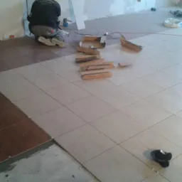 Układanie brązowych i beżowych płytek podłogowych z krzyżykami dystansowymi w Nieszawie, widoczne narzędzia i resztki opakowań.