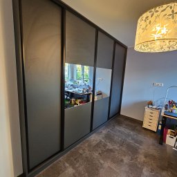 Artex Kuchnie i Wnętrza Natalia Kubiak - Szafa przesuwna z lustrem w szarej ramie, odbijająca biurko z akcesoriami, oświetlona lampą z motywem kwiatowym. Nowoczesny design, widok z perspektywy podłogi.