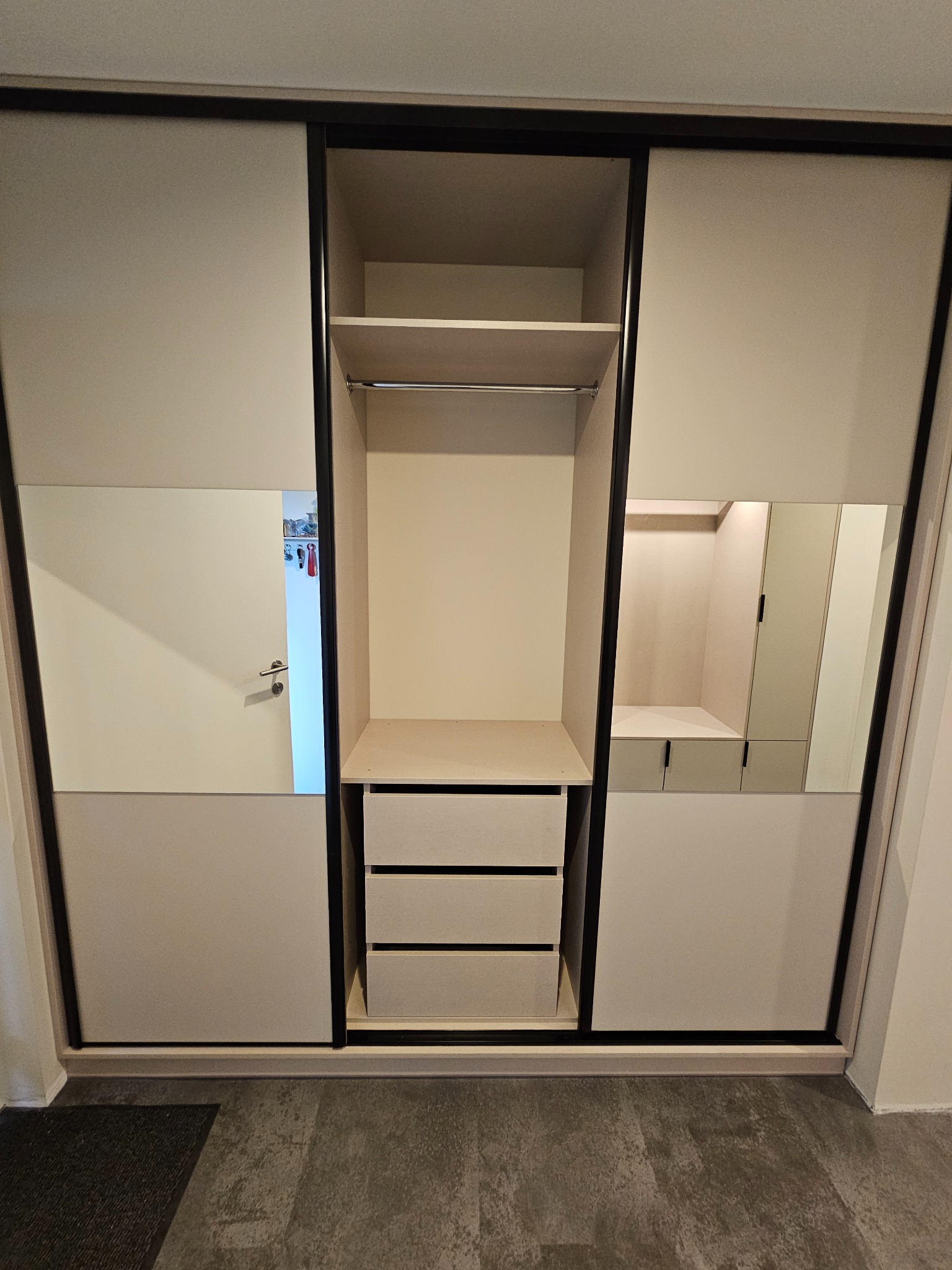 Szafa przesuwna z lustrami i szufladami w neutralnej kolorystyce, widoczna wnęka z półką i drążkiem, nowoczesny design, szare panele podłogowe.