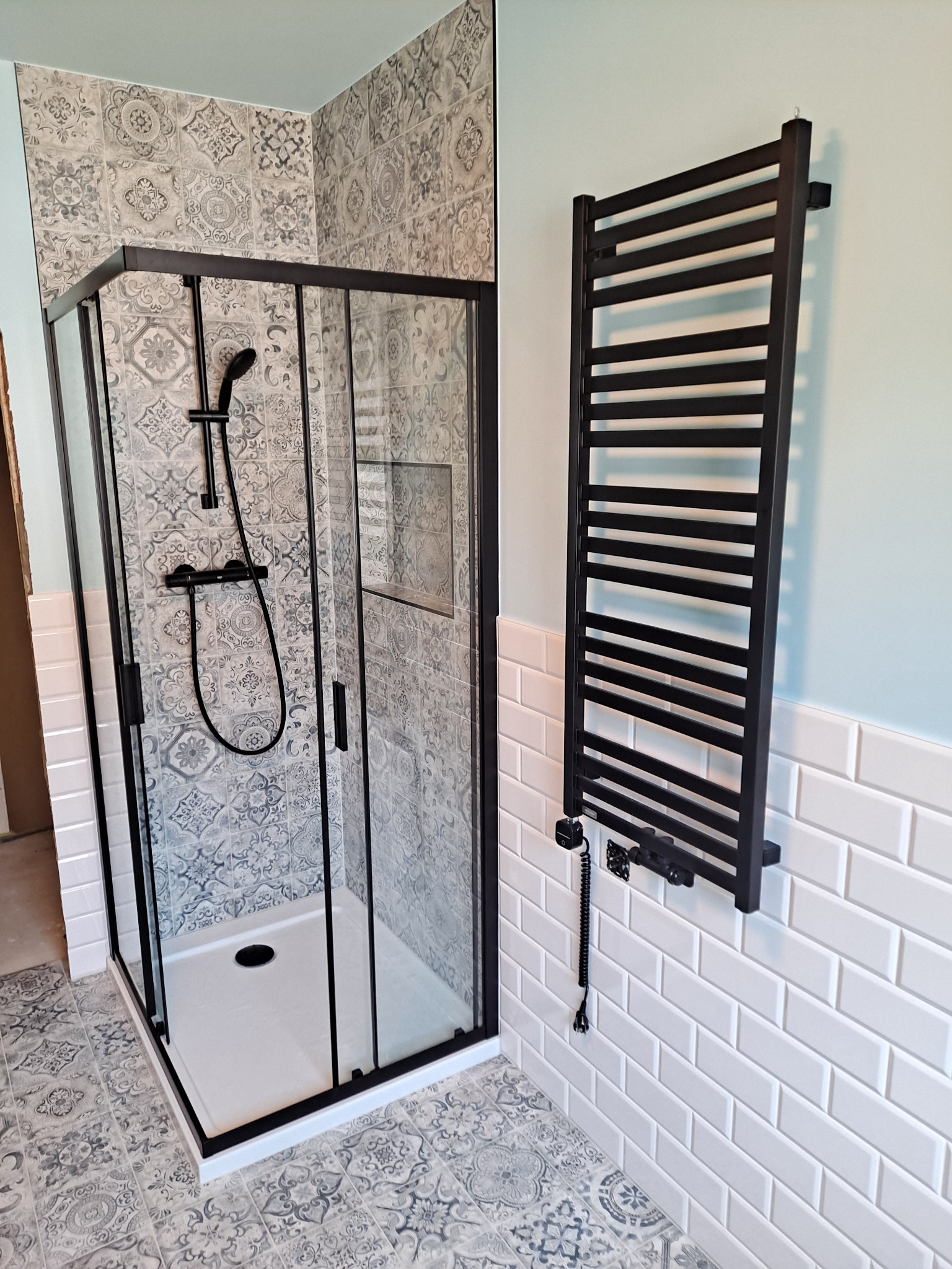 Nowoczesna kabina prysznicowa z czarną ramą i grzejnikiem drabinkowym w wykończonej łazience z dekoracyjnymi płytkami podłogowymi i ściennymi.