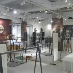 Wnętrze sklepu w Tarnowie w trakcie prac wykończeniowych: surowe ściany, odsłonięte instalacje pod sufitem, metalowe konstrukcje regałów i manekinów, drabina oparta o ścianę, podłoga zabezpieczona...