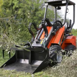 Pomarańczowa maszyna z czarnym osprzętem zbiera gałęzie na trawiastym terenie, widok z perspektywy operatora.