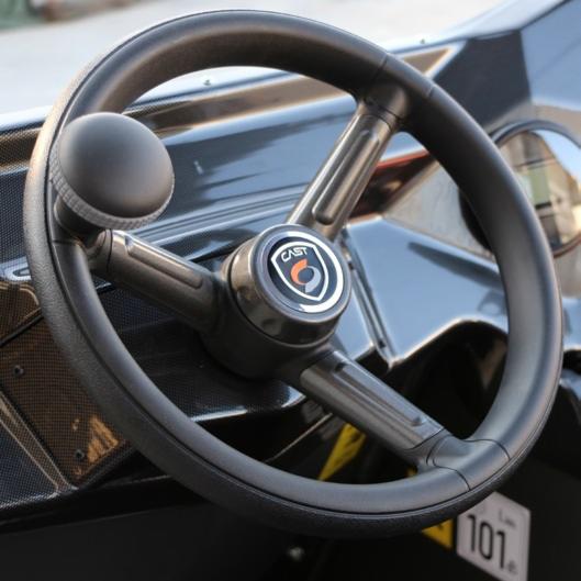 Czarna kierownica miniładowarki z gałką i logo CAST na tle błyszczącej karoserii i numerem 101.